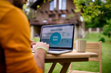 Unrecognizable man with laptop working outdoors in garden, home office concept.