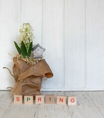 Multicolored inscription "Spring" on wooden cubes, spring decor and white blooming hyacinth in craft paper