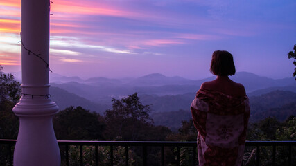 beautiful woman silhouete looking at pink and purple sky sunrise with mountain view