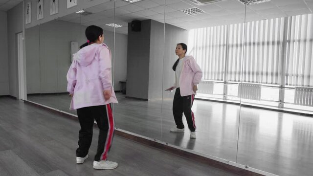 Attractive asian woman with headphones dancing hip hop in studio against mirror