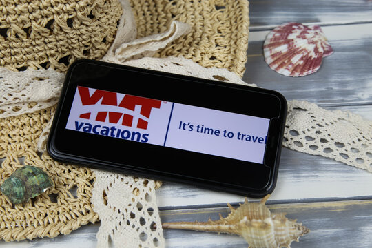 Viersen, Germany - March 1. 2021: Closeup of smartphone with logo lettering of ymt vacations travel agency with sun hat and shells on wood table