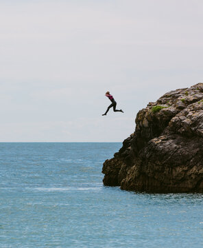 Teenage girl leaping from rocks into the sea.