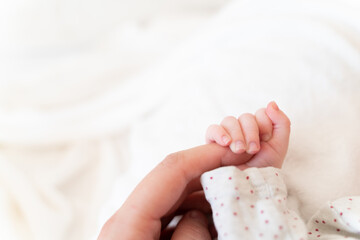 tiny, cute hand of a little caucasian newborn baby girl or boy on a white soft and cosy background, with pink skin, playfully holding its mother's finger. symbol of love and happiness of a family  