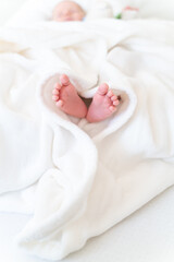Obraz na płótnie Canvas Mother's/Father's loving hand holding tiny, cute, bare feet of a little caucasian newborn baby girl/boy. Baby lying on a white soft and cosy blanket, sleeping. Symbol of love, happiness of a family 