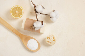 baking soda in wooden spoon, soap, luffa, lemon and cotoon flower on beoge background copy space