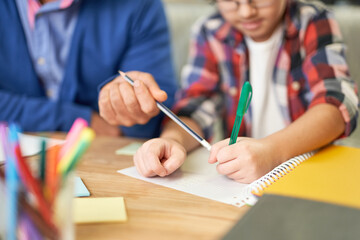 Close up of hands of middle aged latin father helping his son, school child with homework while sitting together at the desk at home - obrazy, fototapety, plakaty