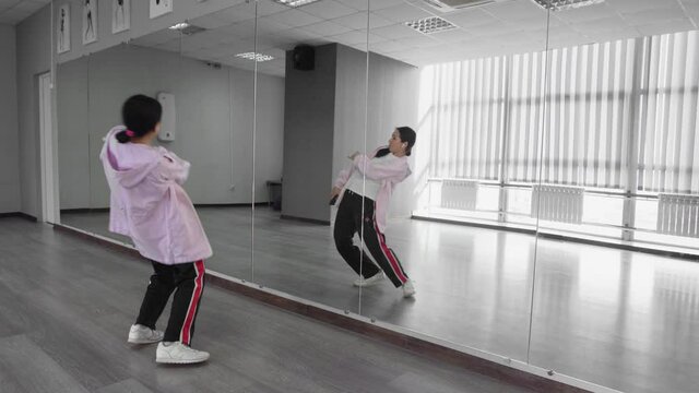 Attractive asian woman with headphones dancing hip hop in studio against mirror