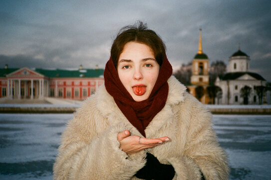 Portrait of a girl with a bleeding tongue in the snow with Slavic architecture behind her