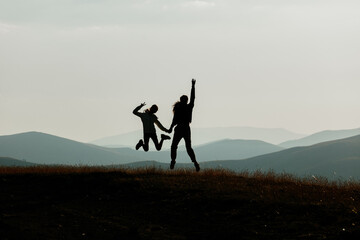 Mother and child silhouettes jumping on mountain at sunset