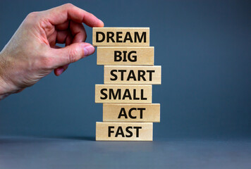 Dream big start small symbol. Words 'dream big start small act fast' on wooden blocks on a beautiful grey background. Businessman hand. Business, motivational and dream big start small concept.