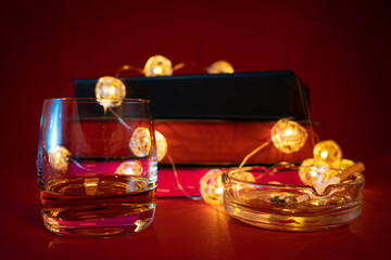 Glass of whiskey and burning cigarette with books in background