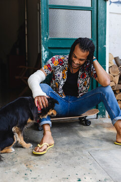 Handsome young man sitting on the skateboard caresses his dog