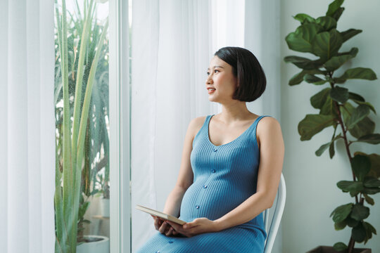 Pregnant asian woman looking at ultrasound scan of baby and touching her belly,