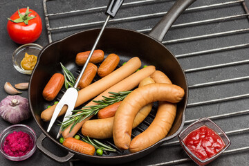 Sausages and sprigs of rosemary in frying pan on metal grate
