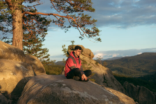 a guy sitting in a high rock at sunset