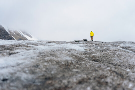 a tourist in a yellow plaque walks on a glacier
