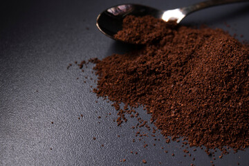 gold teaspoon in a pile of ground or instant coffee on dark background