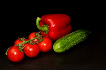 Fresh organic diet vegetables on a black background. Branch of cherry tomatoes, red paprika and cucumber