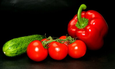 Fresh organic diet vegetables on a black background. Branch of cherry tomatoes, red paprika and cucumber. Space for your text