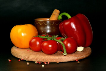 still life branch of cherry tomatoes, red paprika, garlic and spice, plate with ketchup on wooden board on a black background