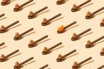 Pattern made of chocolate spoons with small chocolate golden color egg on it, one spoon with slice of tangerine. Lovely beige background.