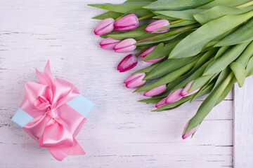 Romantic gift box tied with big pink bow and spring tulips on white wooden surface. Mother s day or Easter holiday minimalist concept.