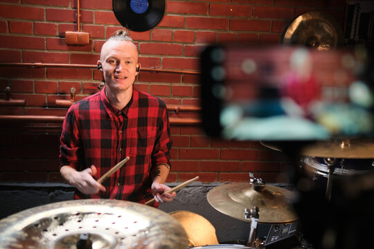 Drummer guy plays online and records video on smartphone.