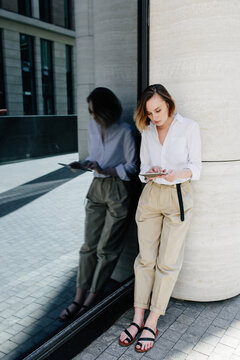 Stylish woman using tablet standing near business center on city street
