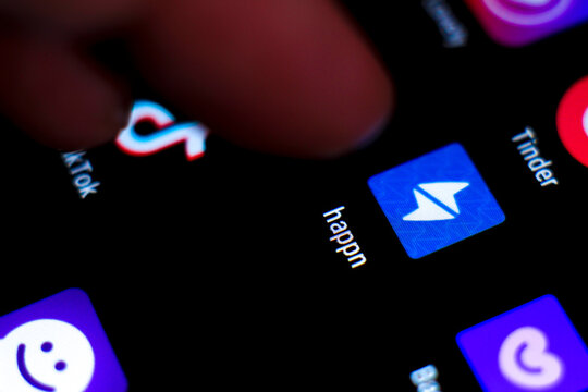 Finger pressing Happn app icon on black screen