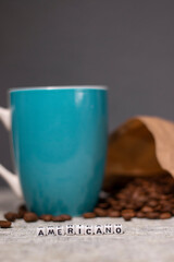 blue cup near coffee beans falling from paper bag and word AMERICANO written with little white cubes in front
