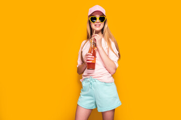 Lovely woman with cold drink standing on yellow background