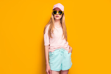 Fototapeta premium Elegant blonde woman wearing fashion cap, sunglasses enjoying sun on yellow summer background