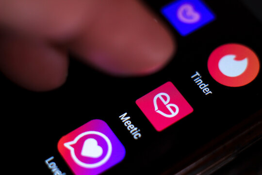 Finger pressing Meetic app icon on black screen