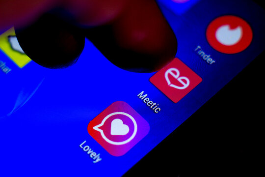 Finger pressing Meetic app icon on blue screen