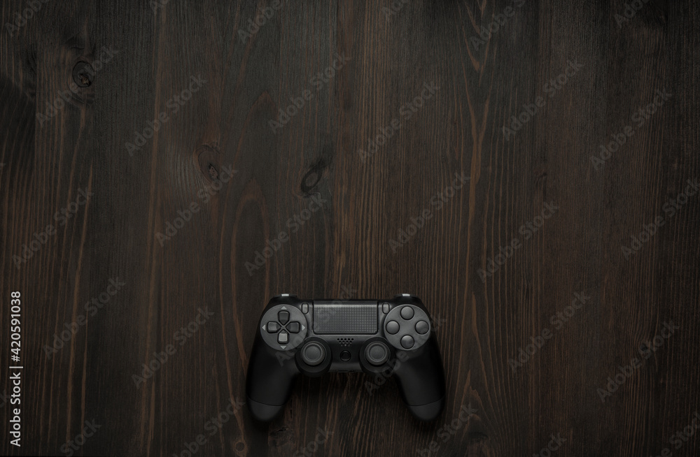 Wall mural Modern black gamepad on a dark wooden background. Game concept with copy space for text.