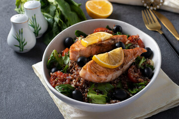 Salad with quinoa, salmon, spinach, black olives, lemon and cherry tomatoes in a plate on gray background. Healthy eating. Close up