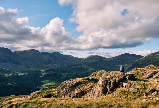 Female walker on Hard Knott looking towards Sca Fell at sunset. Lake District, Cumbria, UK.