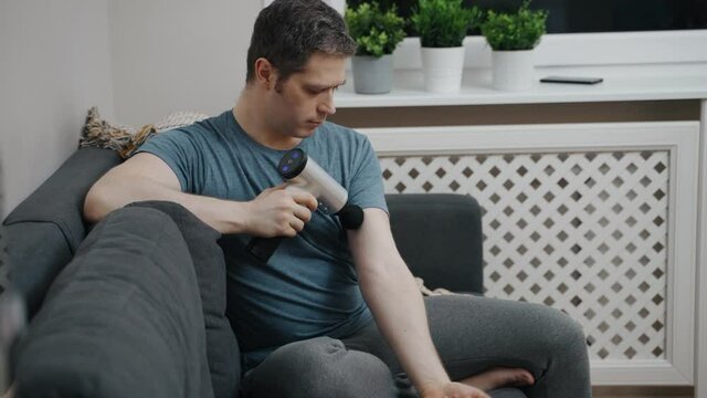 Man massaging arm with massage percussion device at home.