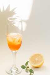 Cold refreshing drink with lemon orange slices by the glass on white background on directly sunlight with shadows - 420594450