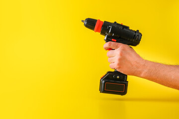 Cordless battery powered screwdriver on yellow background with cropped male hand holding tool for...