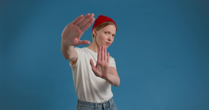 Dissatisfied blonde female in shirt showing stop sign with outstretched hand and saying no, dont show me this, deny reject concept. indoor studio shot, blue background, chroma key