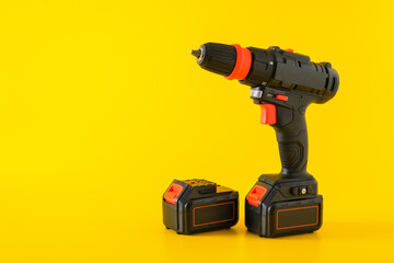 Modern black cordless screwdriver, drill with recharge battery on yellow background, copy space for text