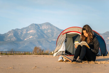 Joven mujer leyendo un libro al amanecer junto al mar.  - obrazy, fototapety, plakaty