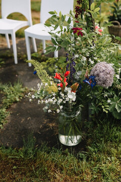 wild flowers in a vase on the grass with white chairs in the back