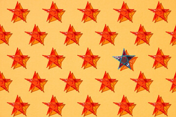 One blue star standing among other red stars on orange color background