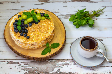 Homemade Napoleon cake (Mille-feuille) decorated with grapes, blueberries and mint leaves on a wooden table.