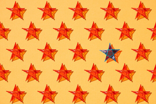 One blue star standing among other red stars on orange color background