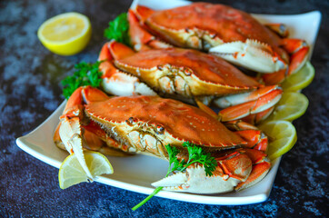 Three boiled crabs with lemon and parsley on a white plate.
