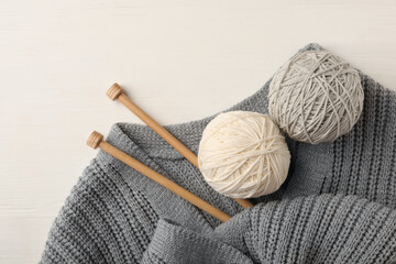 Woolen yarns, knitting needles and sweater on white wooden background, flat lay