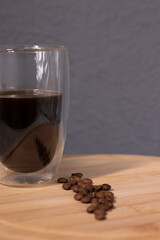 americano in a double bottom glass near coffee beans on wooden plate. coffee break